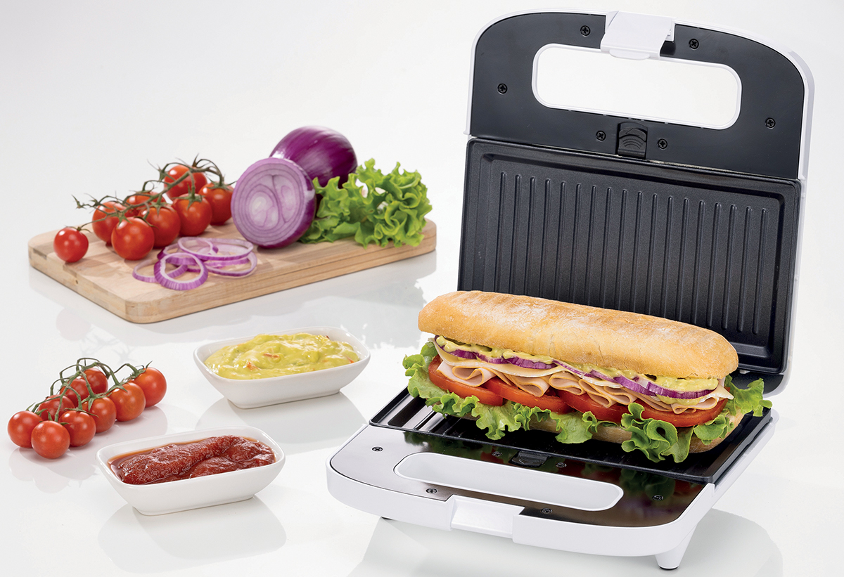 Απεικονίζεται η τοστιέρα με ένα σάντουιτς και τα υλικά του σκορπισμένα στην επιφάνεια ενός τραπεζιού